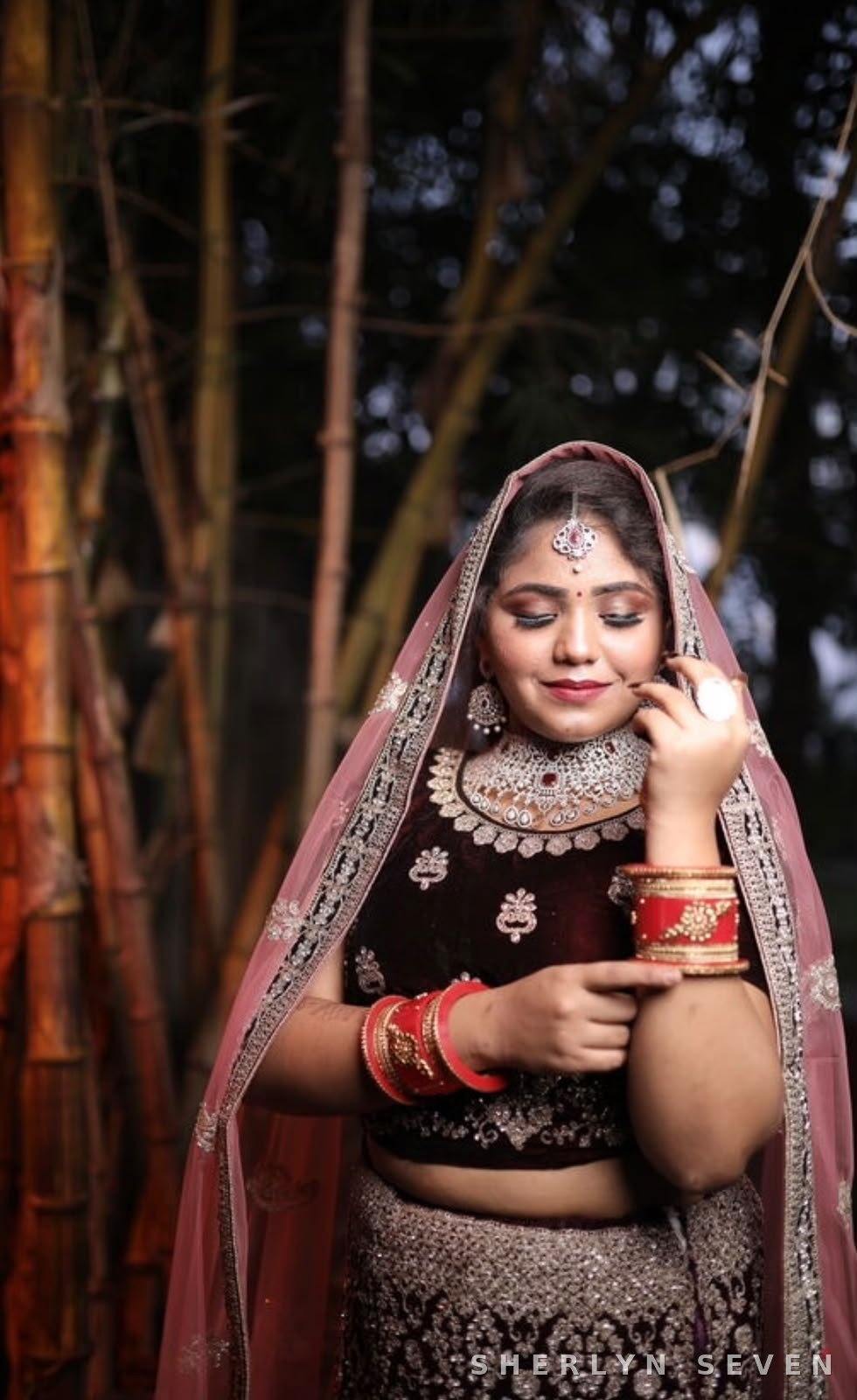 Bridal look in a pink-veiled lehenga with heavy jewellery against a bamboo backdrop