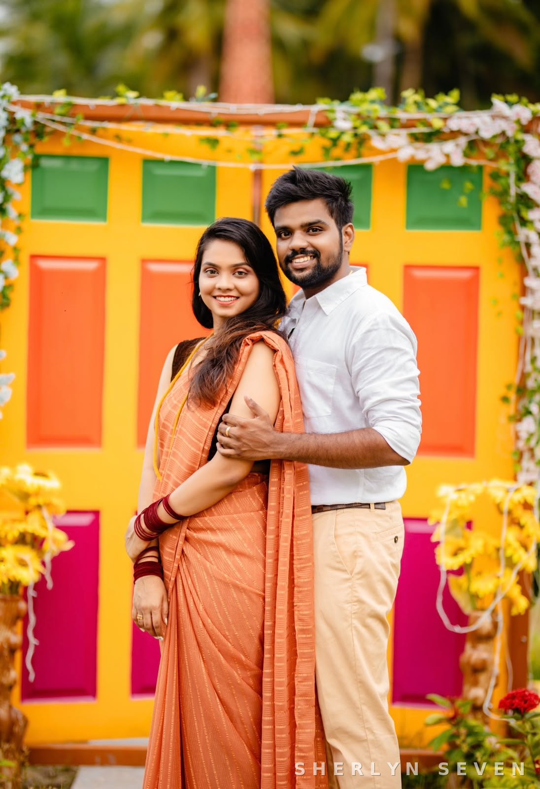 Engagement look in an orange saree against a colourful backdrop